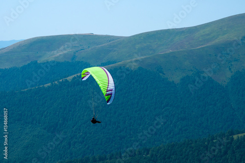 Paraglider flies paraglider over the tops of the mountains in summer sunny day. Carpathians, Ukraine.