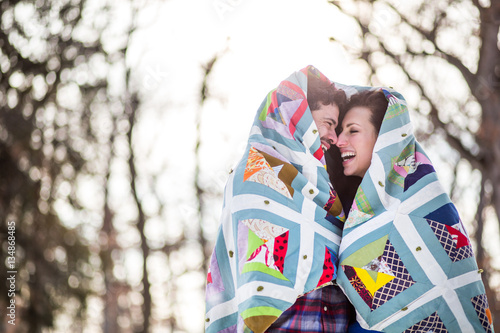 Couple wrapped in patchwork quilt, laughing photo