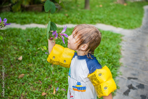Tableau sur toile Young boy holding a tropical stem in the garden looking and smelling the flower