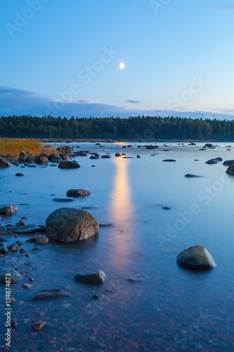 Colorful seascape with moon and lunar path with rocks at night in summer