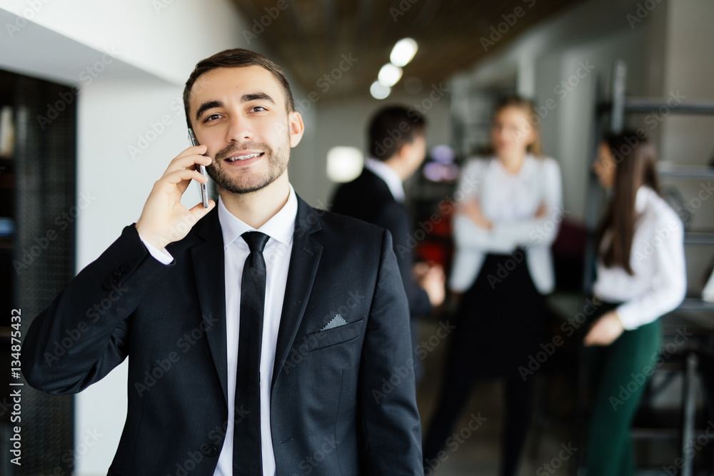 Business man speak on mobile phone in front of discussing colleagues in office. Business man speak on mobile phone in front of discussing colleagues in office.