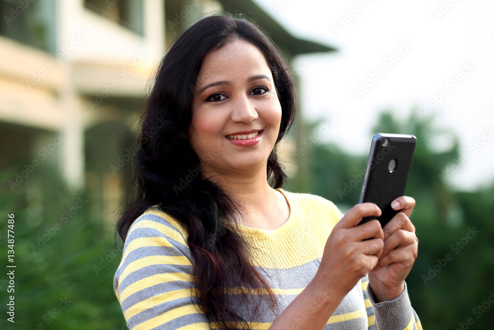 Portrait of a smiling woman texting with her cellphone at outdoo