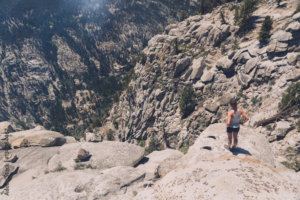 A young caucasian woman looks down into a deep granite gorge in the California mountains