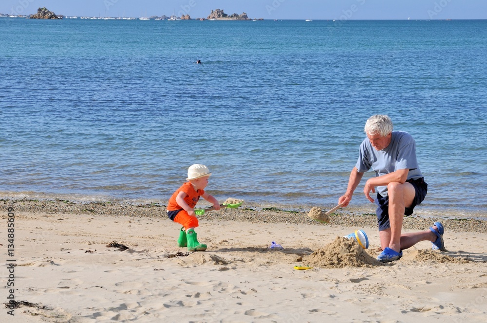 Un grand-père joue dans le sable avec son petit-fils sur une plage de Bretagne Un grand-père joue dans le sable avec son petit-fils sur une plage de Bretagne