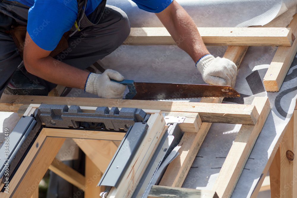 Skylight installation. Roofer builder worker use saw to cut a wooden beam Skylight installation. Roofer builder worker use saw to cut a wooden beam