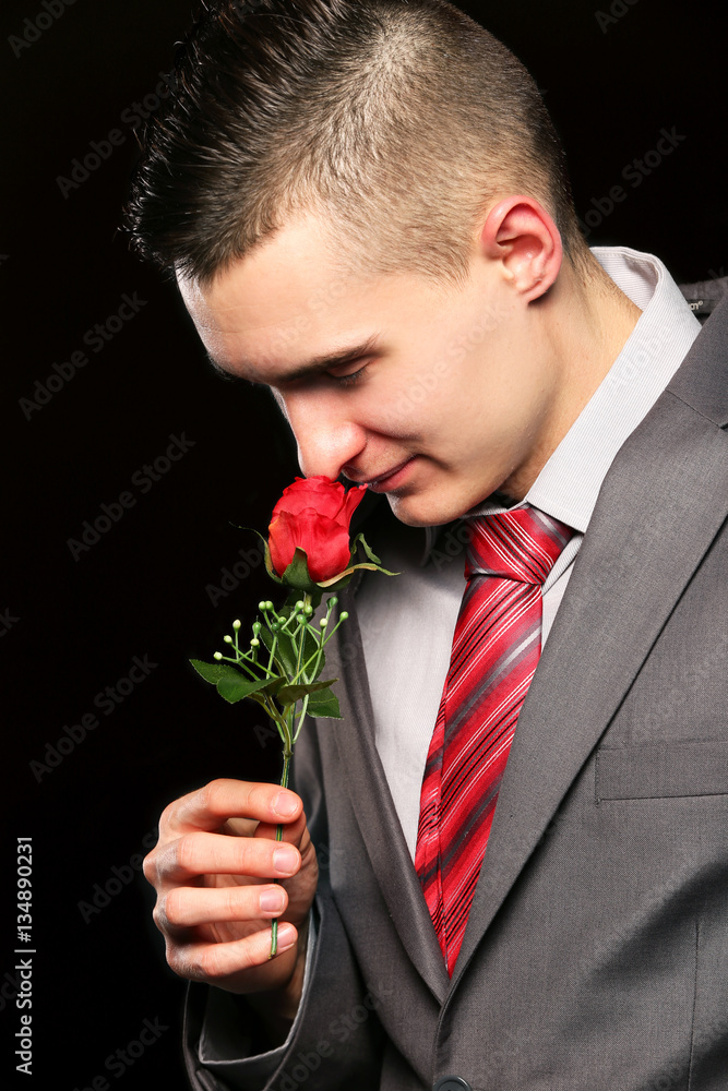young man in a nice suit smells a red rose young man in a nice suit smells a red rose