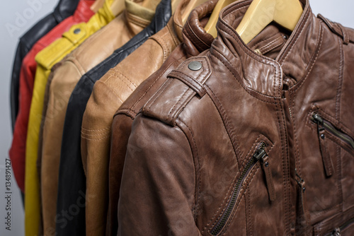 Different color leather jacket hanging on rack on white background