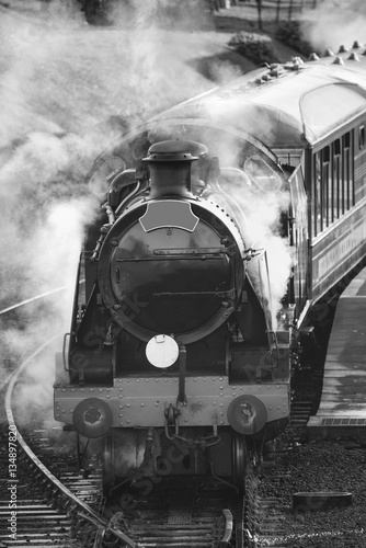 Restored Victorian era steam train engine with full steam in bla