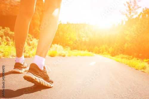 Legs in sport shoes on road at sunrise closeup.