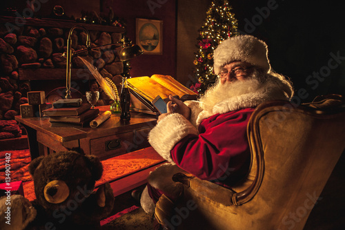 Santa Claus looks back over his shoulder and smiles, showing off his smartphone.