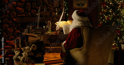 Santa Claus uses a massive quill pen to double-check his naughty list.
