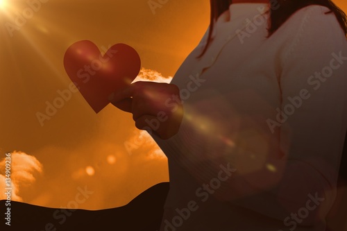 Composite image of midsection of woman holding heart shape paper