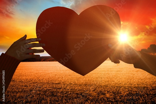 Composite image of hands holding orange heart shape paper