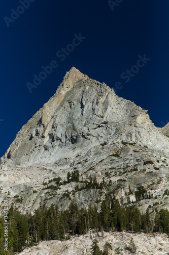 A sharp granite peak rises over a forested valley under a deep blue sky