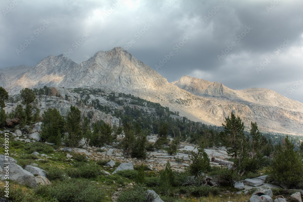 A hanging meadow surrounded by mountains under a stormy sky