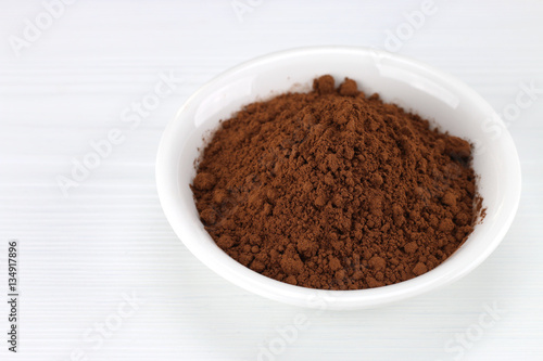 Cocoa powder in white bowl over wooden background
