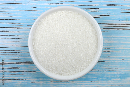 White sugar in white bowl over wooden background