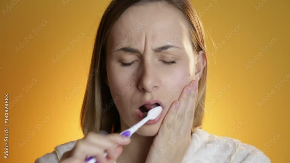 Woman brushing her teeth and smiling against yellow background Woman brushing her teeth and smiling against yellow background