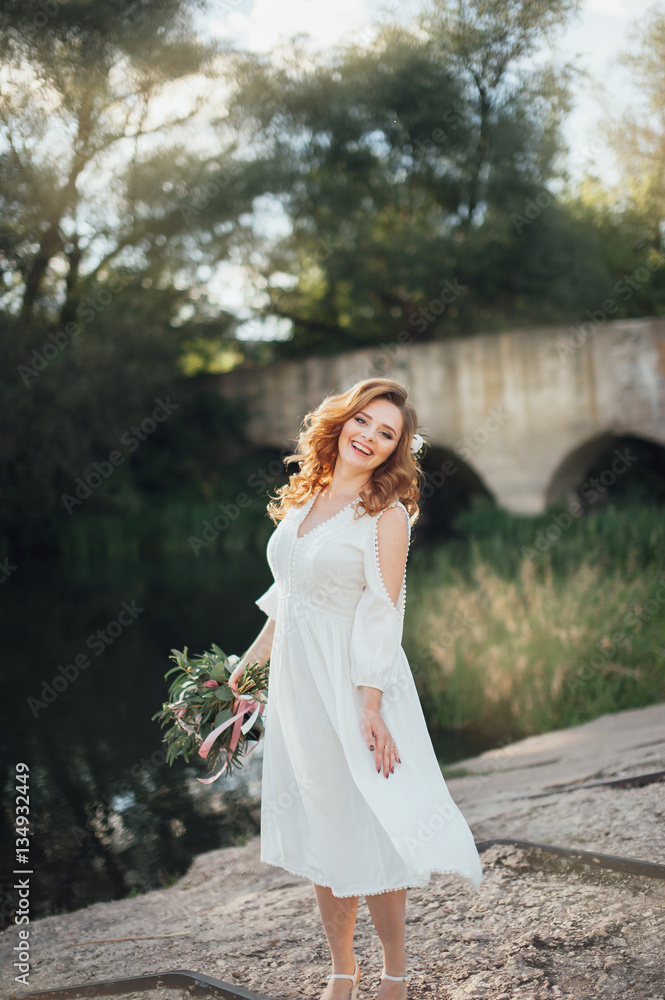 Beautiful bride with a big bouquet of different flowers posing on nature background