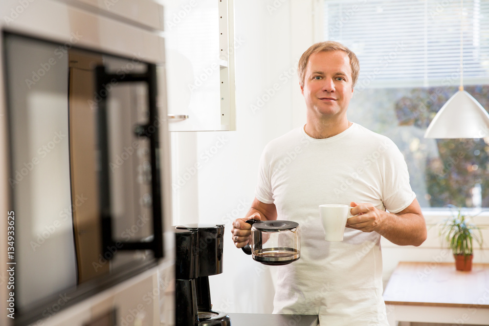 Man in the kitchen pouring a mug of hot filtered coffee from a glass pot. Having breakfast in the morning Man in the kitchen pouring a mug of hot filtered coffee from a glass pot. Having breakfast in the morning