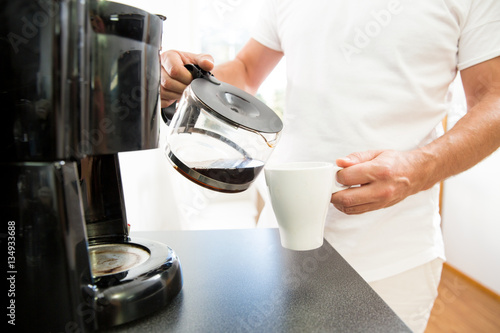 Man in the kitchen pouring a mug of hot filtered coffee from a glass pot. Having breakfast in the morning