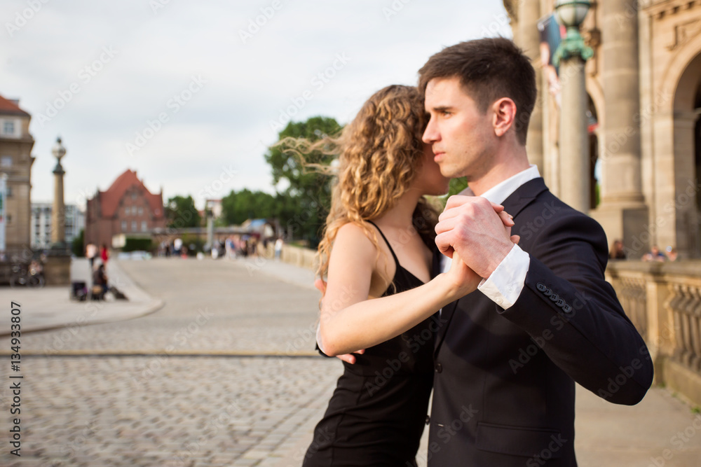 two young people - a man in black suit and a woman wearing black dress - dancing tango outside; a musician is playing romantic songs; focus on the dancers hands two young people - a man in black suit and a woman wearing black dress - dancing tango outside; a musician is playing romantic songs; focus on the dancers hands
