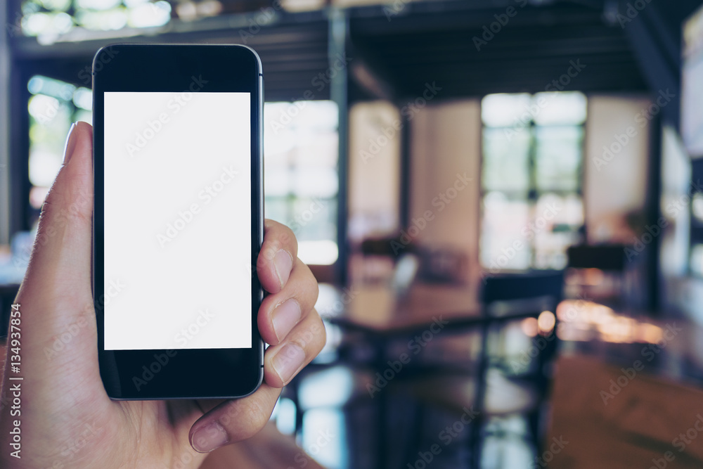 Mockup image of hand holding black mobile phone with blank white screen in cafe
