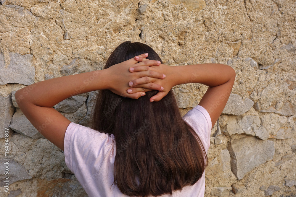 girl with long hair leaning against a wall with his hands behind his ...