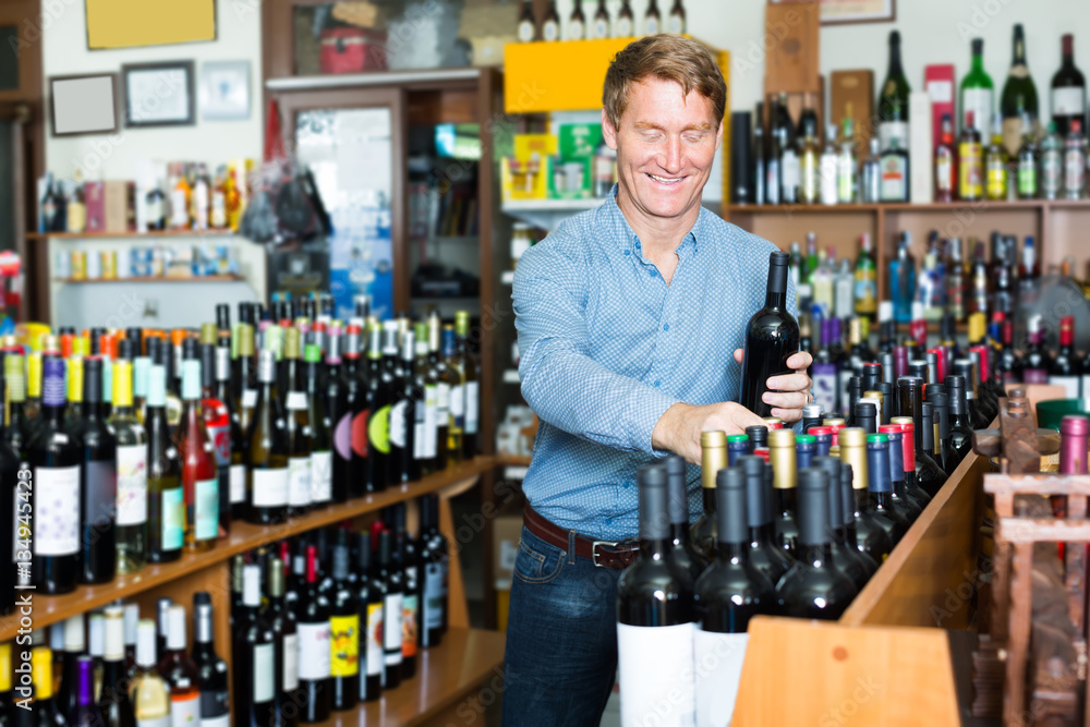 happy middle-aged man customer buying bottle of wine