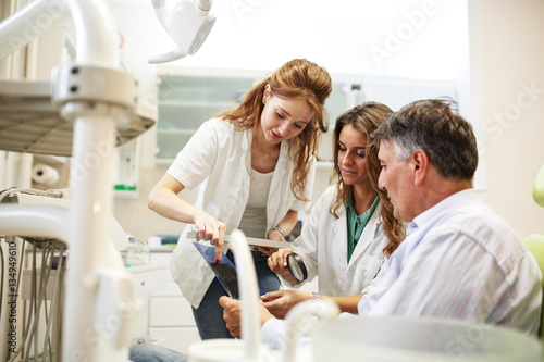 Dentist and her female assistant in dental office talking with senior patient and preparing for treatment.|Examining x-ray image.