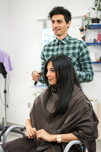 Beautiful young woman is sitting in hairdressing salon. The hairdresser is standing behind her and preparing to work.
