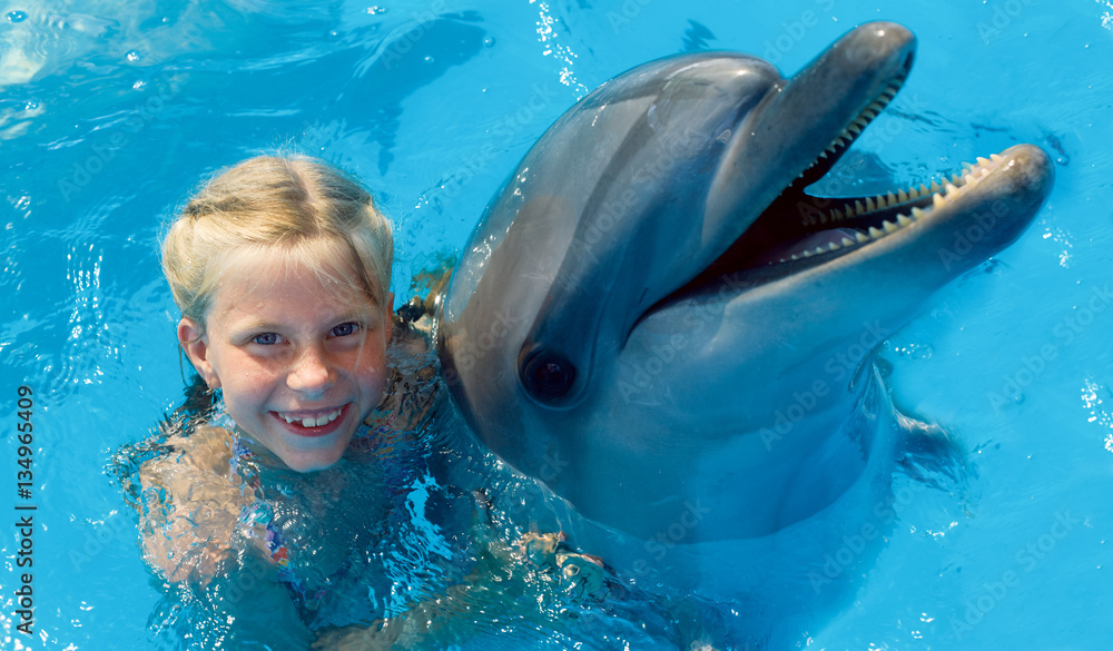 Fototapeta premium Szczęśliwe dziecko i delfiny w błękitnej wodzie. Terapia wspomagana delfinami