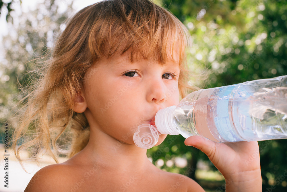 The little girl with curly golden hair pleasure drinks water fro The little girl with curly golden hair pleasure drinks water fro