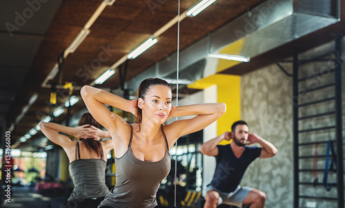 Atractive athletes doing squats in fitness studio.  