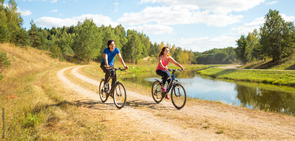 Naklejka premium Young Happy Couple Riding Bicycles by the River. Healthy Lifestyle Concept.
