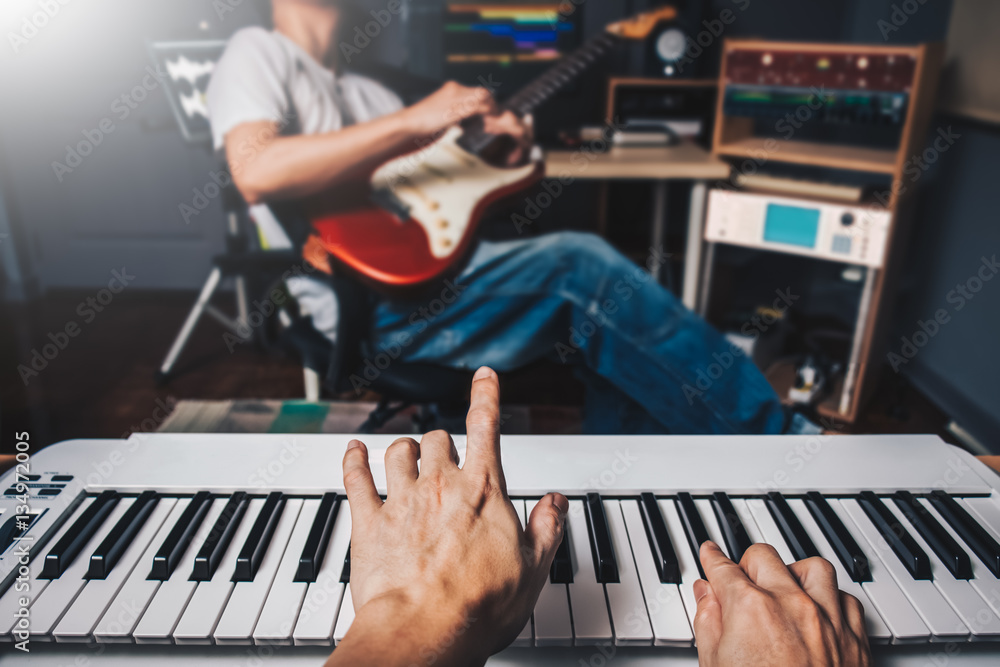 Fototapeta premium music jamming in sound studio, pianist hands playing keyboard on blurred guitar player background. film filter