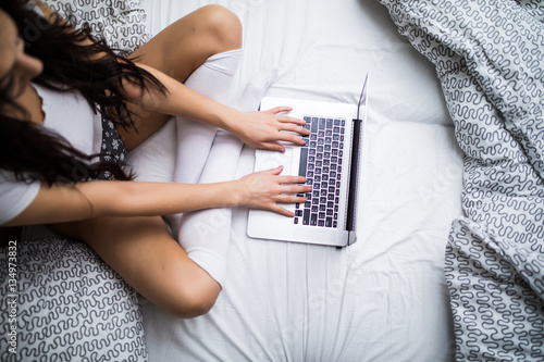 Close up of woman typing on kayboard laptop in bed photo