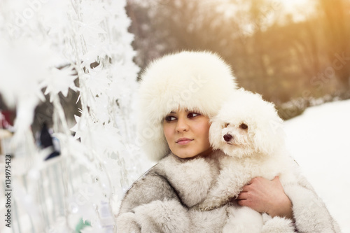 Beautiful woman in the winter time with her dog. Woman wearing a winter coat. Lens flare in the background.
