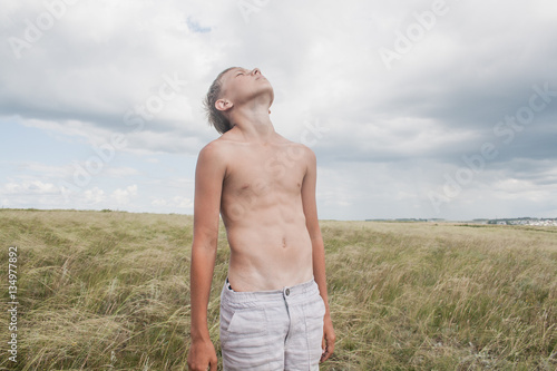 young boy stands in a field. boy in shorts. boy stands in the desert. feather in the field. boy looking up at the sky. dreamer