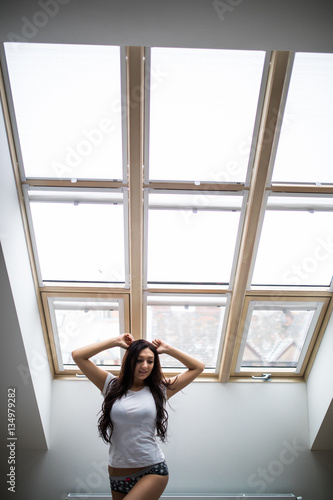 Woman standing near the window while stretching near bed after waking up