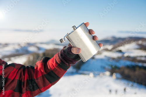 Male hand holding hip flask on a snowy mountain photo