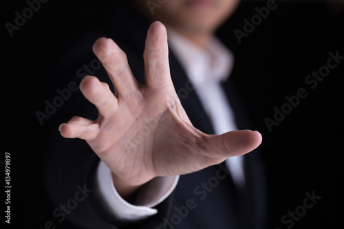A business man in casual black suit gesturing  his palm hand against the camera.