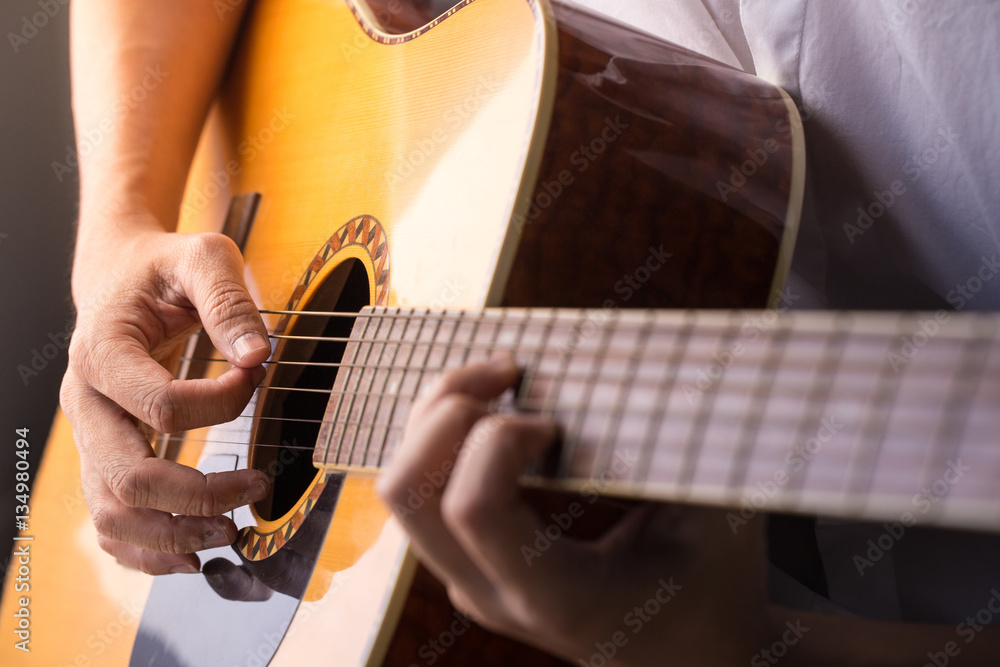 Fototapeta premium Mężczyzna siedzi i gra na klasycznej drewnianej gitarze z bliska na podstrunnicy z akordami.