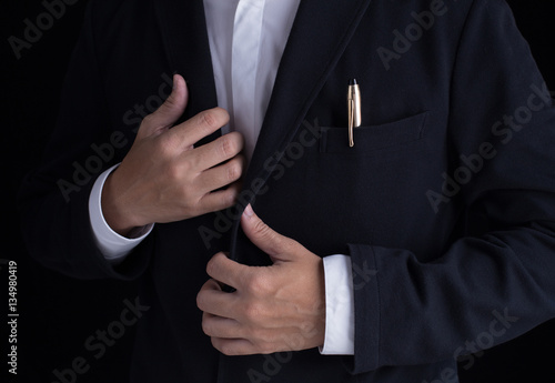 A business man in black suit is dressing up, fastening closing shirt sleeve buttons.