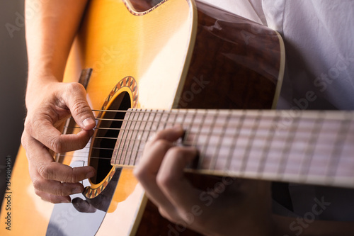 A man sitting and playing classic wooden guitar close up to chord tab fretboard.