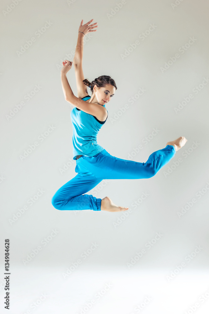 Young beautiful slim girl in blue dancing on a white studio background
