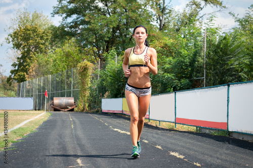 Slender girl with a sports figure in short shorts running around the stadium listening music