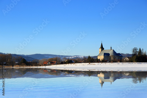 Kościół w górach zimą z odbiciem w wodzie jeziora.