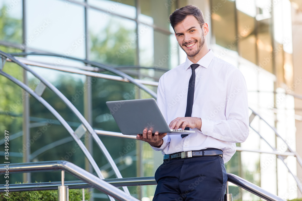 Keep smiling. Confident young man in a suit holding laptop and l Keep smiling. Confident young man in a suit holding laptop and l