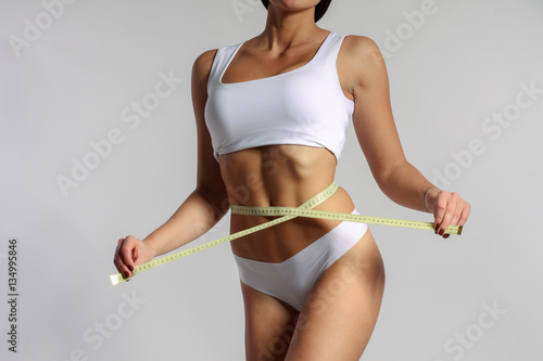 Mid section of woman with sport body measuring her waist with measuring tape, loss weight concept 